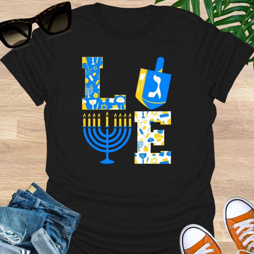 LOVE Hanukkah design with dreidel “O”, menorah “V”, and blue-gold holiday icons on a black unisex tee.