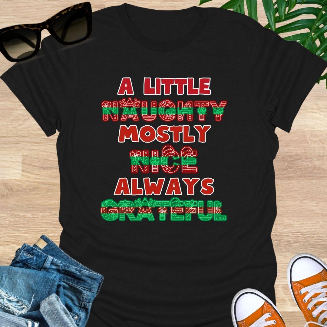 Red-green holiday letters spelling “A Little Naughty, Mostly Nice, Always Grateful” with bows, wreaths, and reindeer on a black unisex tee.