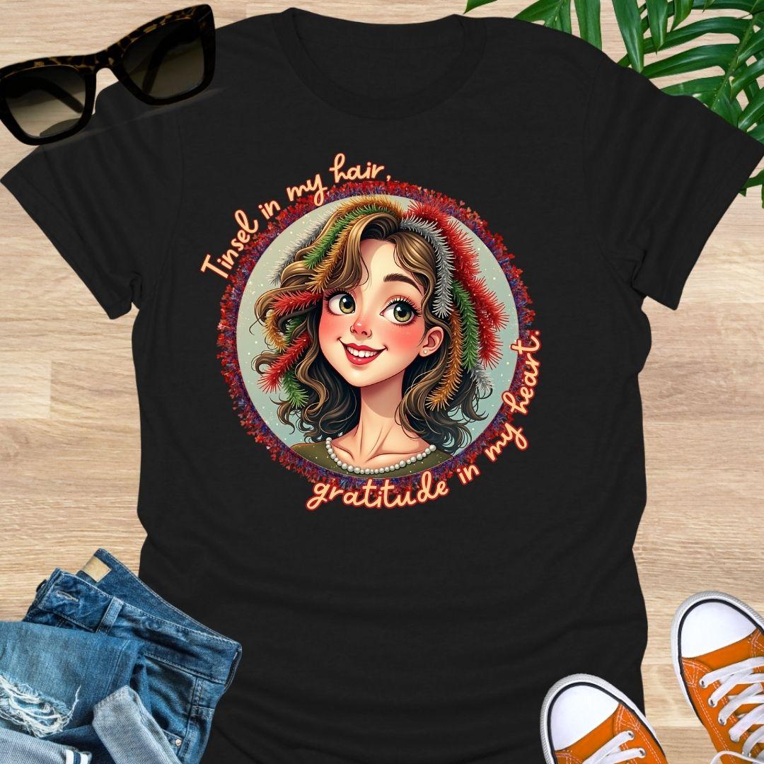 Smiling holiday portrait with colorful tinsel and the phrase “Tinsel in my hair, gratitude in my heart” on a black unisex festive tee.