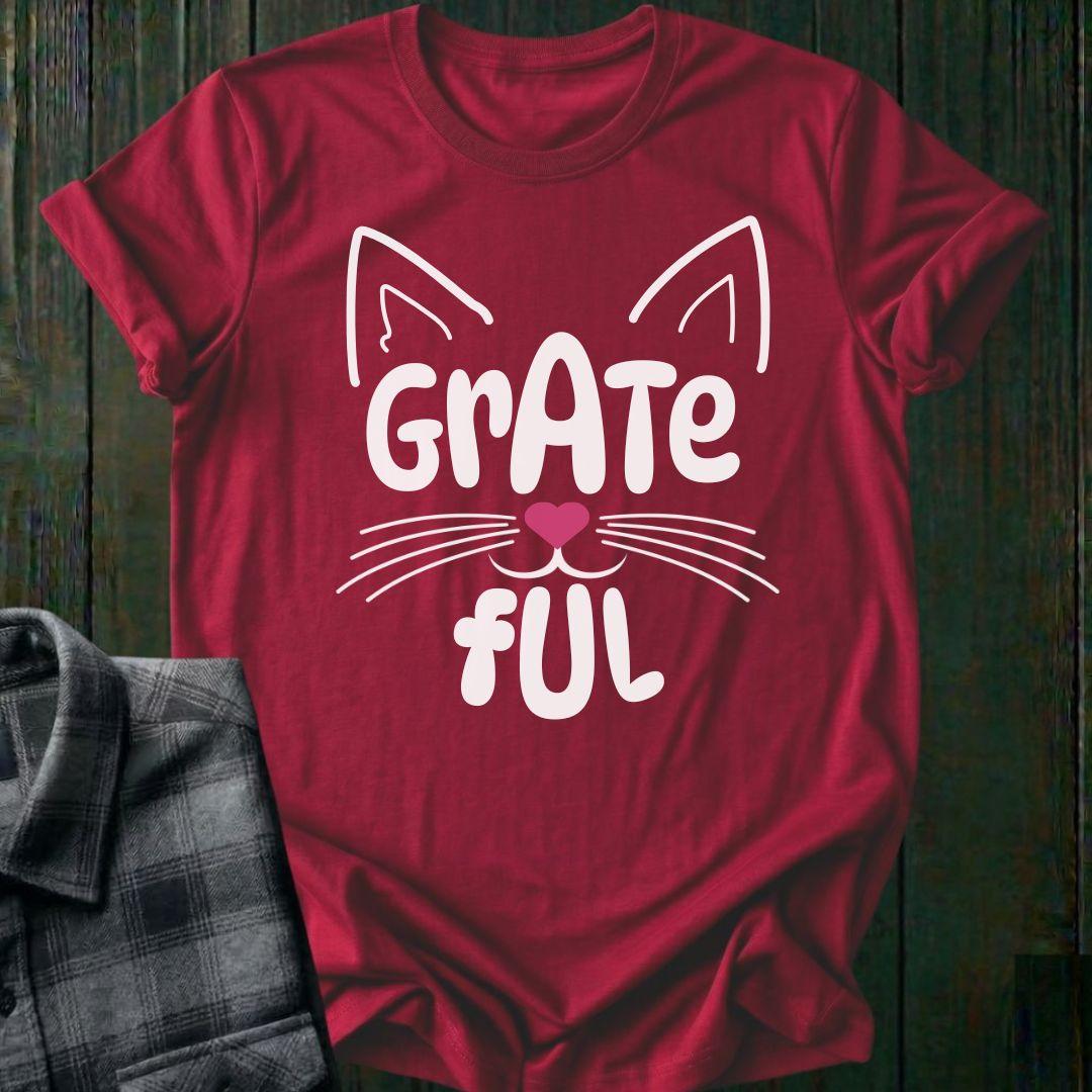 Red t-shirt with a white cat graphic and 'Grate Ful' text on a wooden surface.