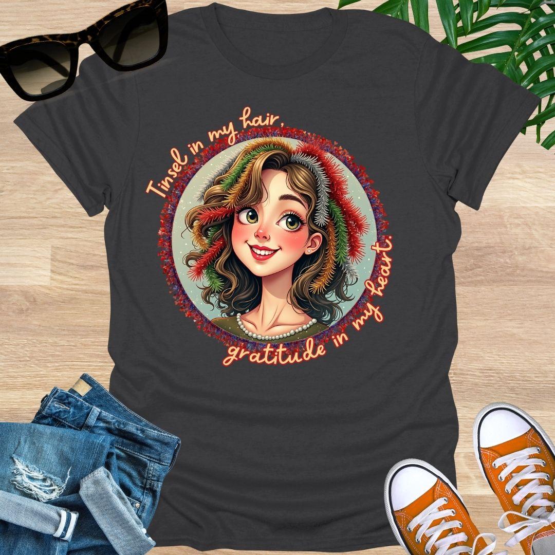 Smiling holiday portrait with colorful tinsel and the phrase “Tinsel in my hair, gratitude in my heart” on a charcoal unisex festive tee.