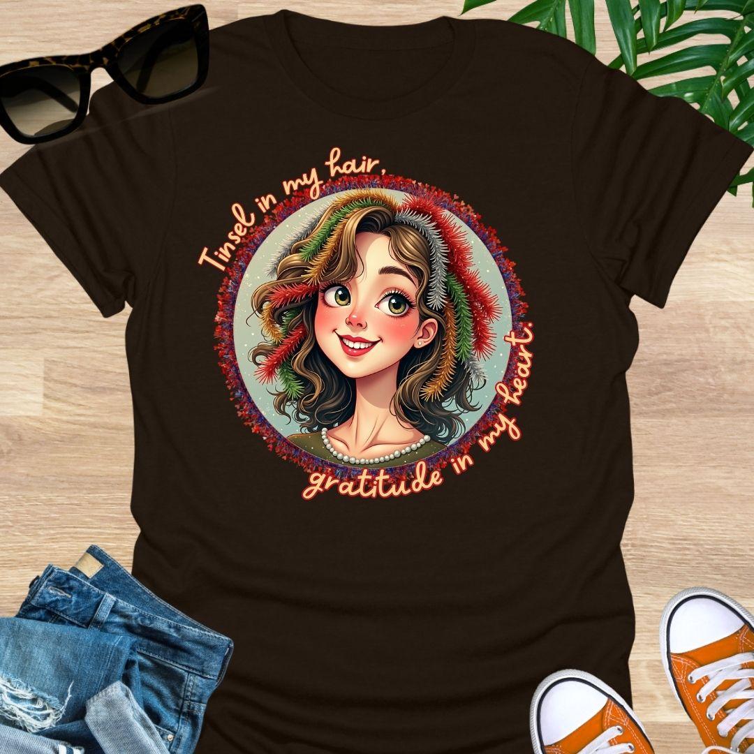 Smiling holiday portrait with colorful tinsel and the phrase “Tinsel in my hair, gratitude in my heart” on a chocolate brown unisex festive tee.