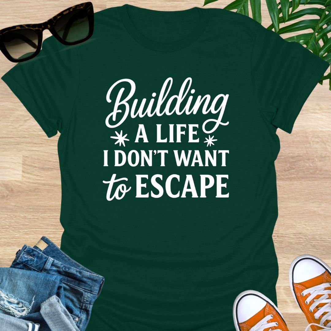 White script with block text: “Building a life I don’t want to escape” on forest green unisex tee.