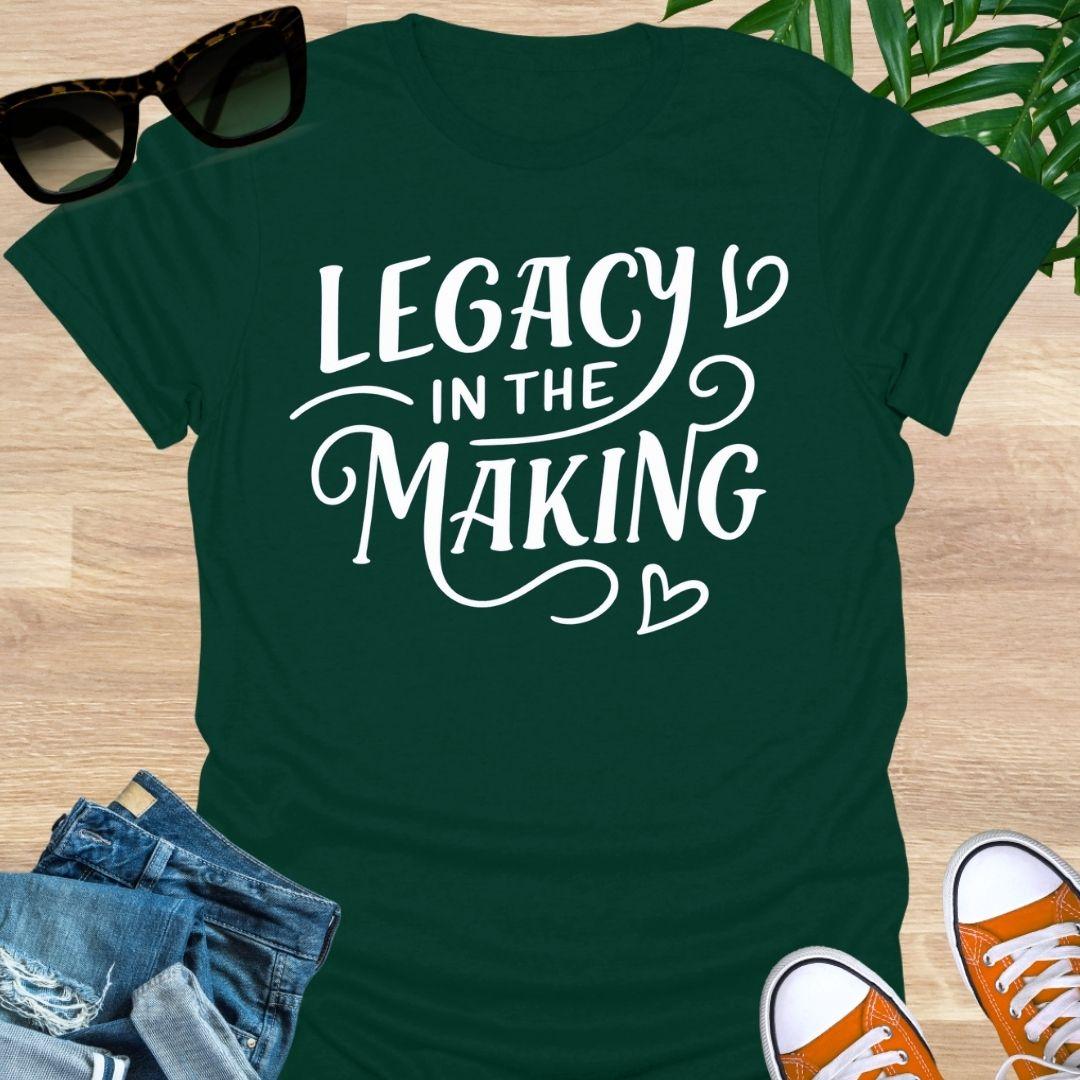 White script “Legacy in the Making” with heart flourishes on a forest green motivational graphic tee.