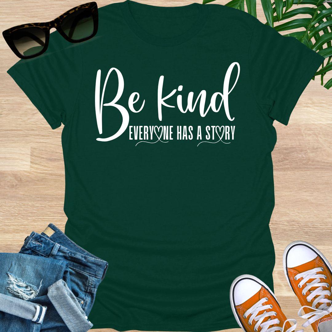 “Be Kind—Everyone Has a Story” in white script with heart loops on a forest green unisex tee.