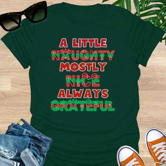 Red-green holiday letters spelling “A Little Naughty, Mostly Nice, Always Grateful” with bows, wreaths, and reindeer on a forest green unisex tee.