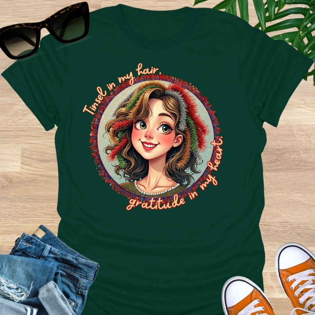 Smiling holiday portrait with colorful tinsel and the phrase “Tinsel in my hair, gratitude in my heart” on a forest green unisex festive tee.