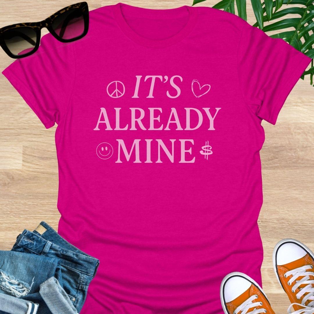 Pink text “It’s Already Mine” with peace, heart, smiley, and dollar icons on a hot pink manifestation graphic tee.