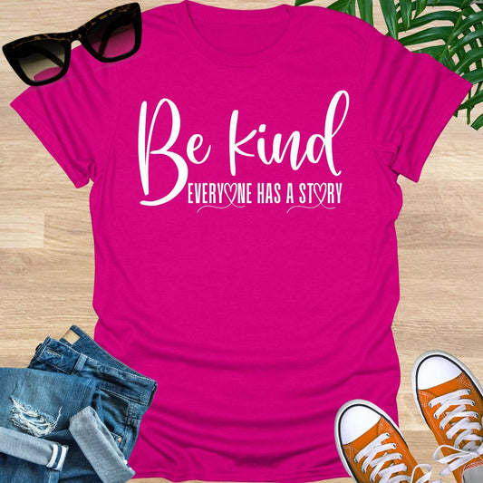 “Be Kind—Everyone Has a Story” in white script with heart loops on a hot pink unisex tee.