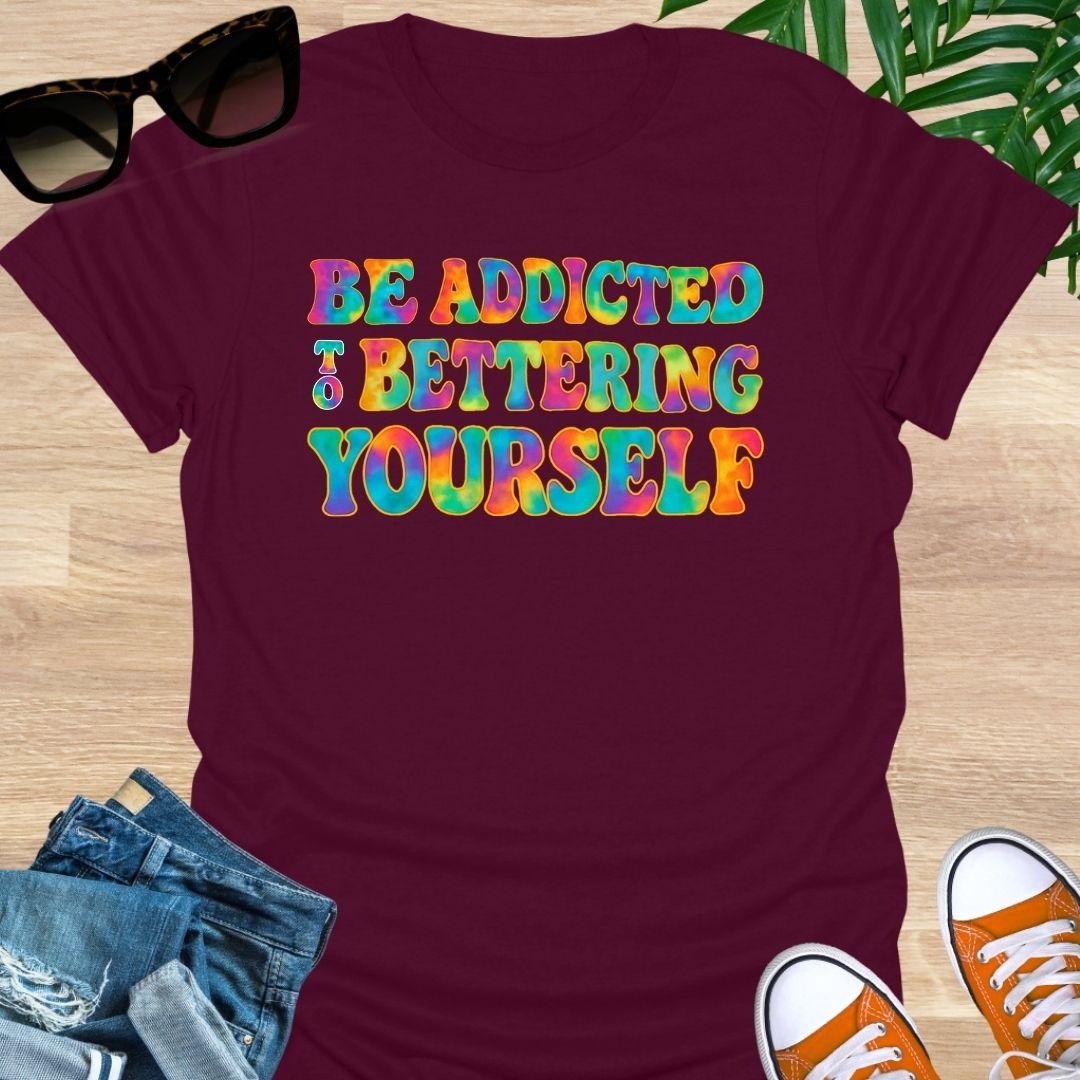 Rainbow tie-dye “Be Addicted to Bettering Yourself” text on maroon unisex growth-mindset tee.