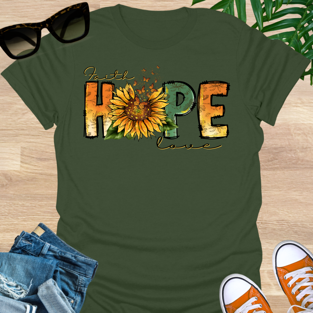 Green t-shirt with a sunflower and monarch butterflies between the words "Faith, Hope, Love" on a unisex graphic tee.