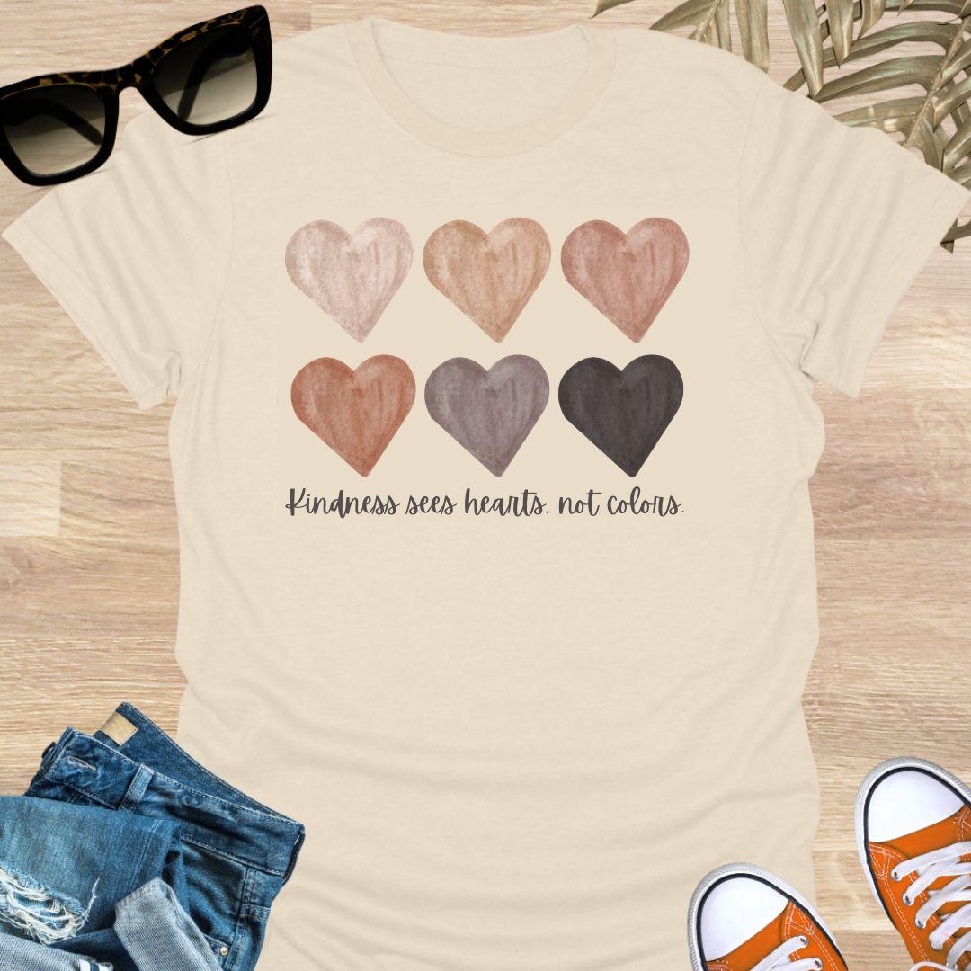 Beige t-shirt with six watercolor hearts in diverse skin tones above the script “Kindness sees hearts, not colors” on a unisex tee.