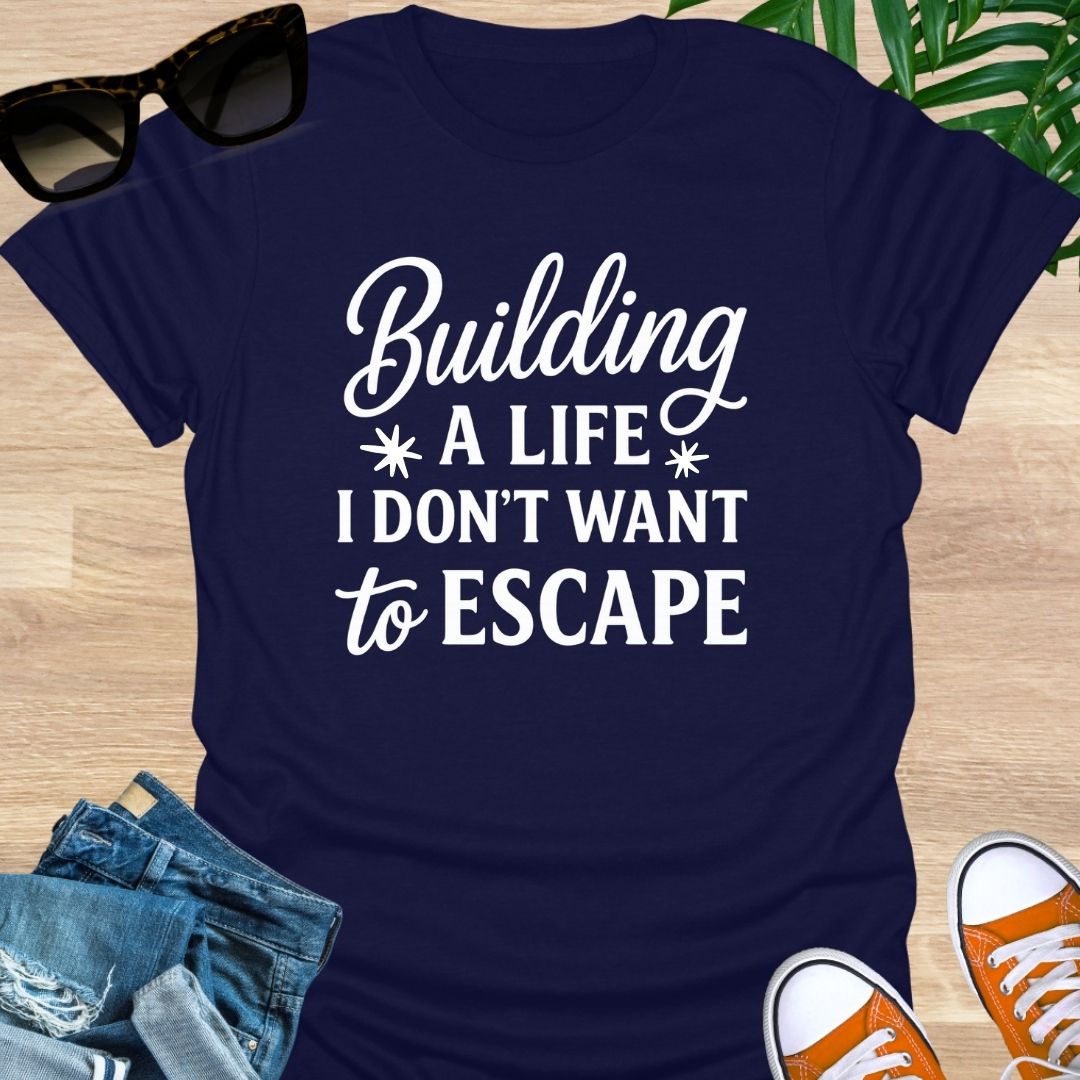 White script with block text: “Building a life I don’t want to escape” on navy unisex tee.