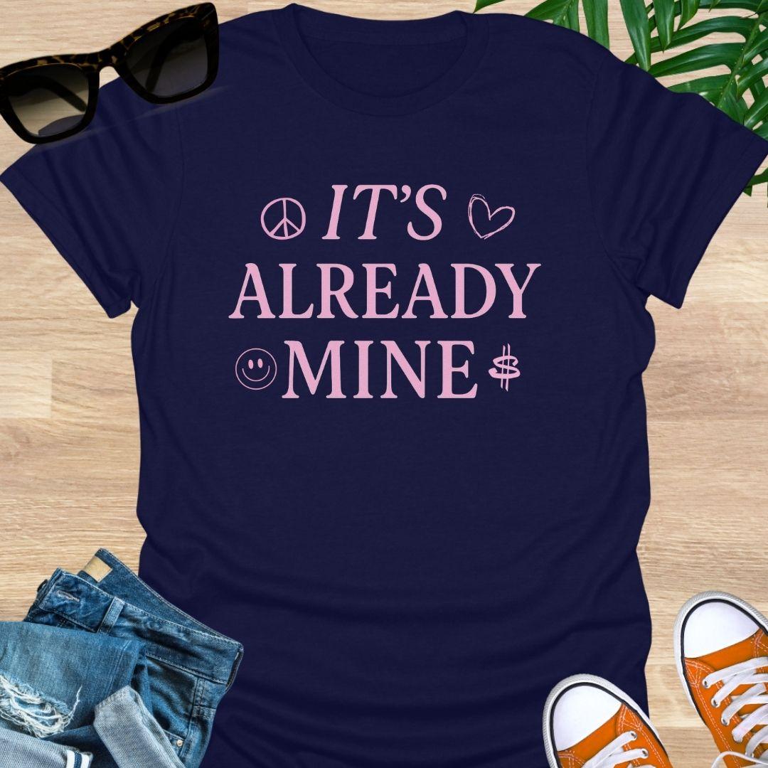 Pink text “It’s Already Mine” with peace, heart, smiley, and dollar icons on a navy manifestation graphic tee.