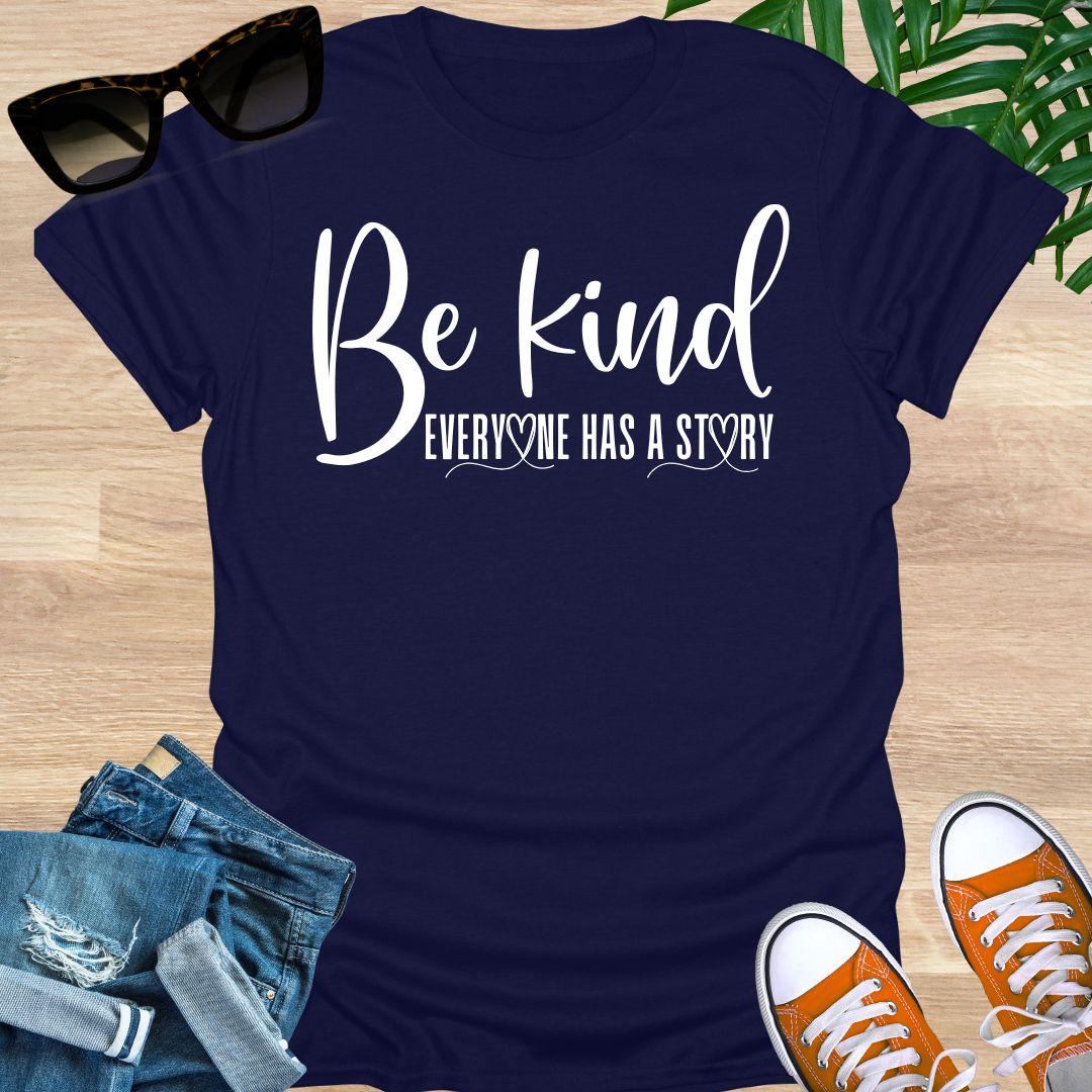 “Be Kind—Everyone Has a Story” in white script with heart loops on a navy unisex tee.