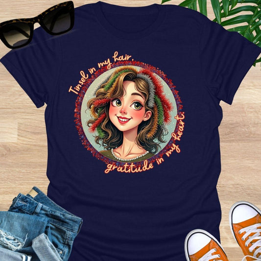 Smiling holiday portrait with colorful tinsel and the phrase “Tinsel in my hair, gratitude in my heart” on a navy unisex festive tee.