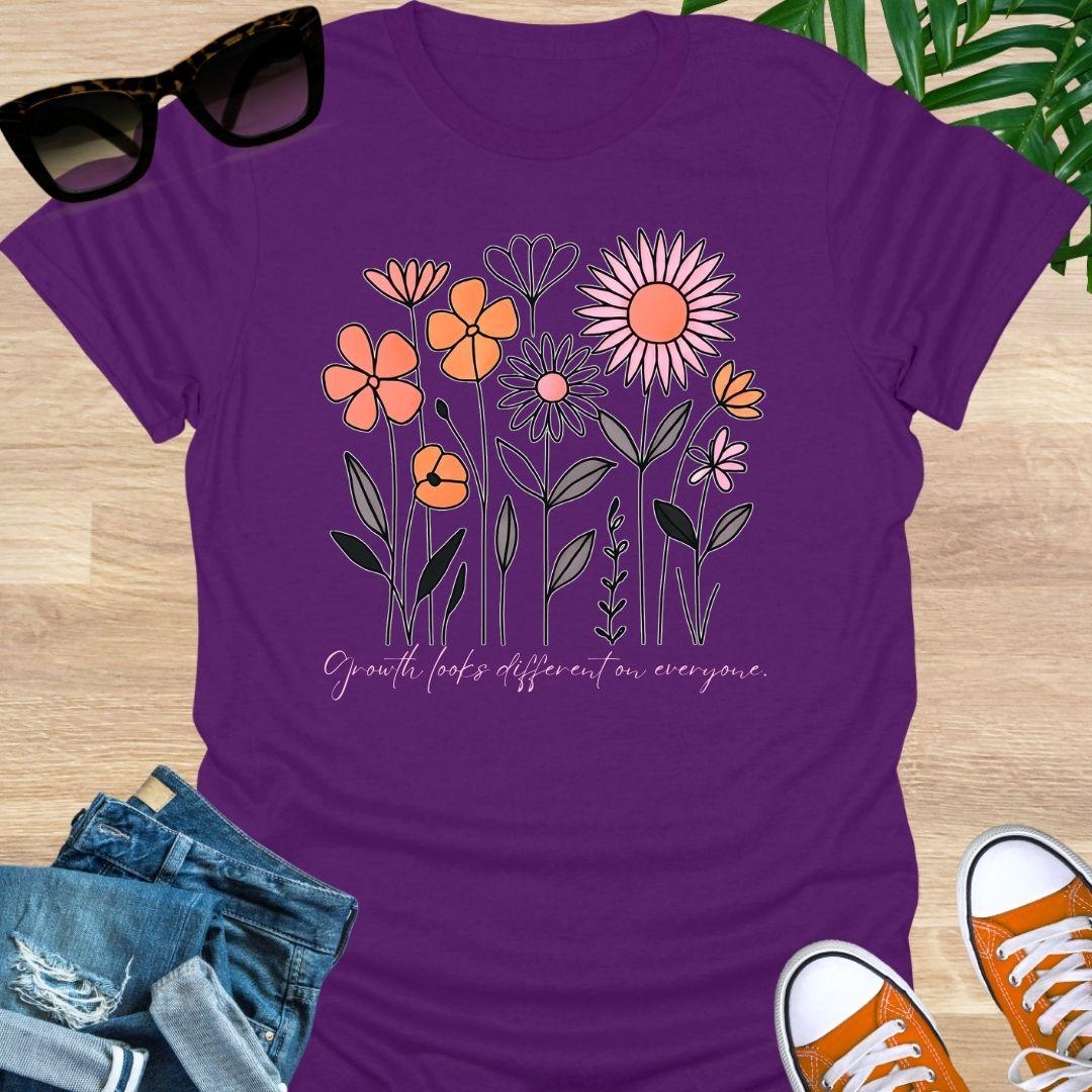 Purple unisex t-shirt. Hand-drawn wildflowers with the script “Growth looks different on everyone”