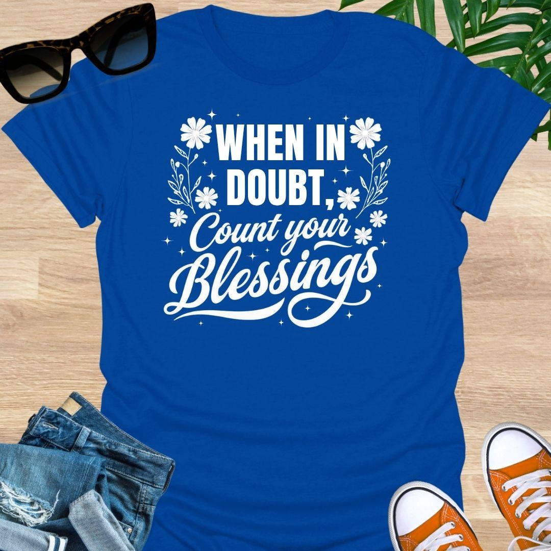 “When in Doubt, Count Your Blessings” in white script with floral and sparkle accents on a blue unisex tee.