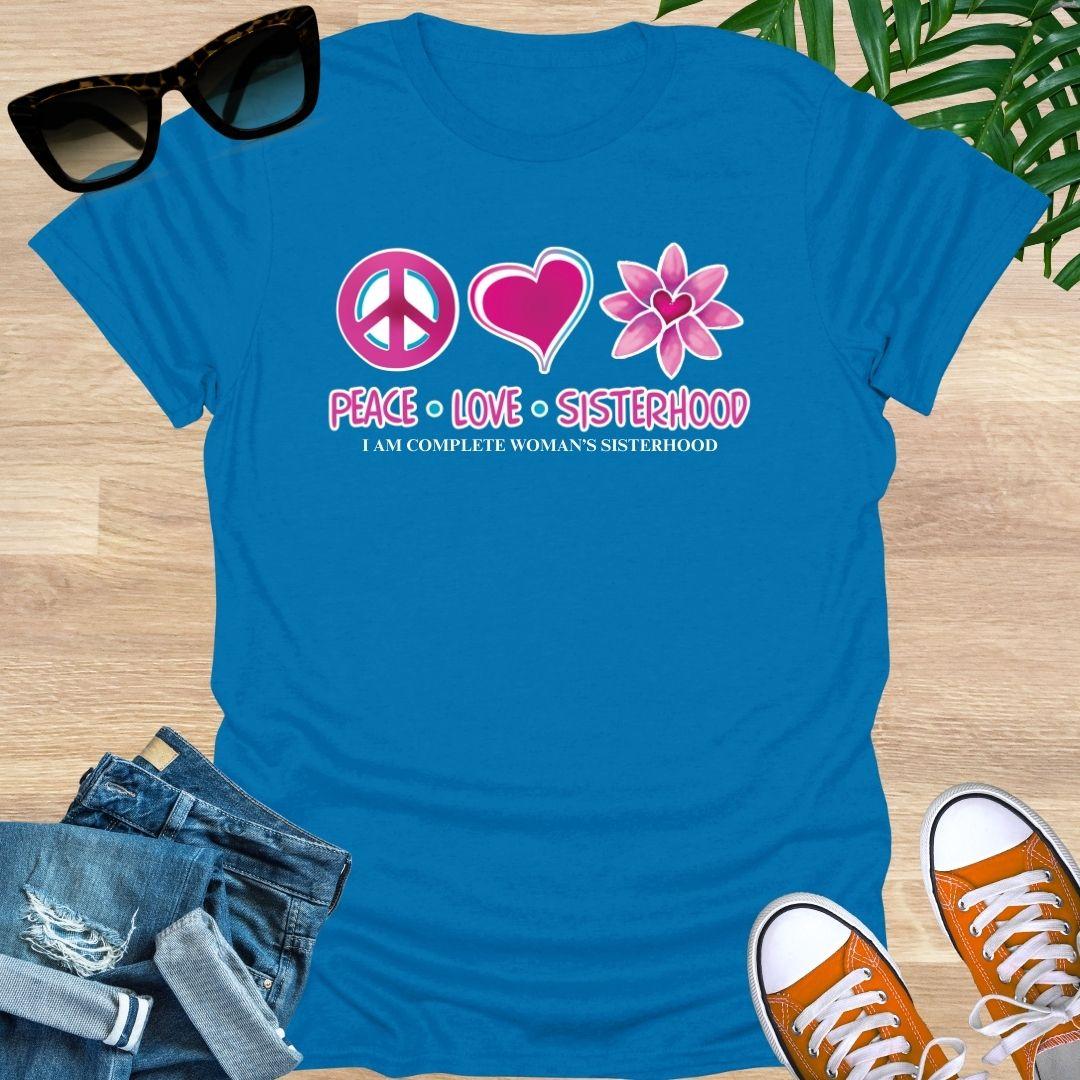 Blue t-shirt with peace, love, sisterhood design on a wooden surface with sunglasses, jeans, and sneakers.