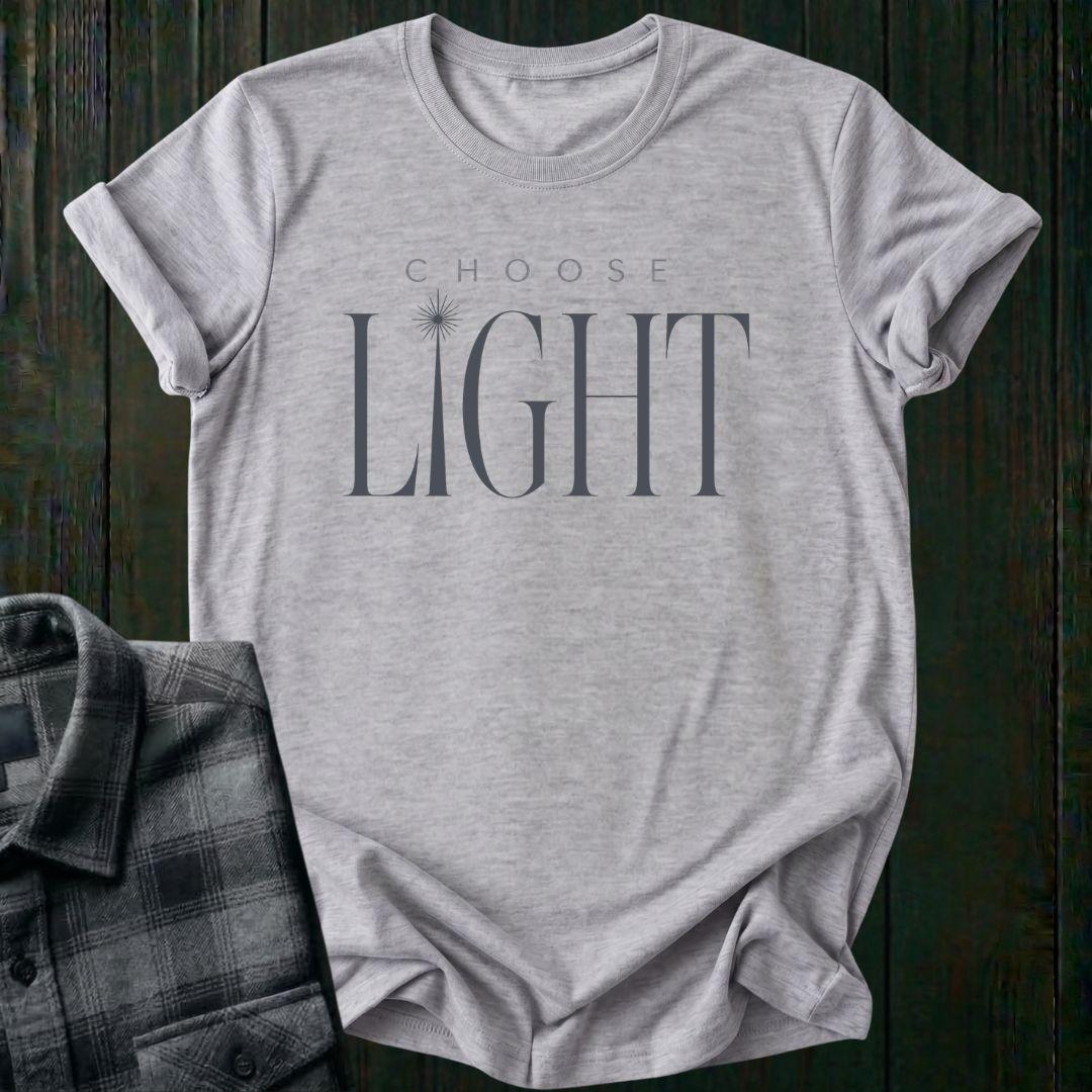 Elegant minimalist typography design featuring the phrase "Choose Light" with a radiant sunbeam replacing the letter I in "Light" on a light gray tee