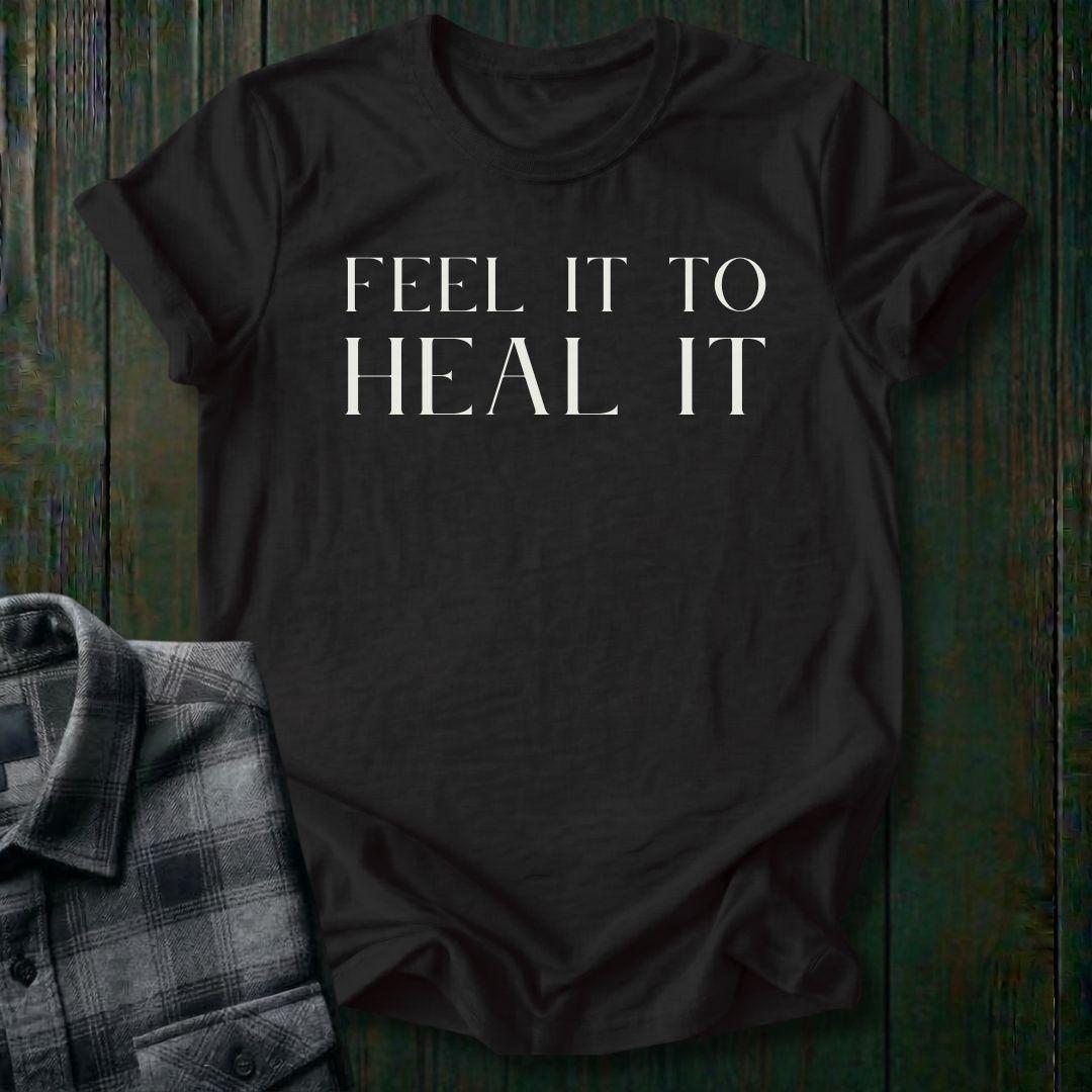 Minimalist typography design featuring the phrase "Feel It to Heal It" in elegant serif lettering on a black tee.