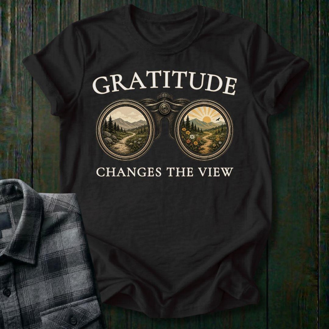 Vintage binoculars graphic showing two landscapes, one ordinary and one bright and colorful, with the phrase "Gratitude Changes the View" on a black tee