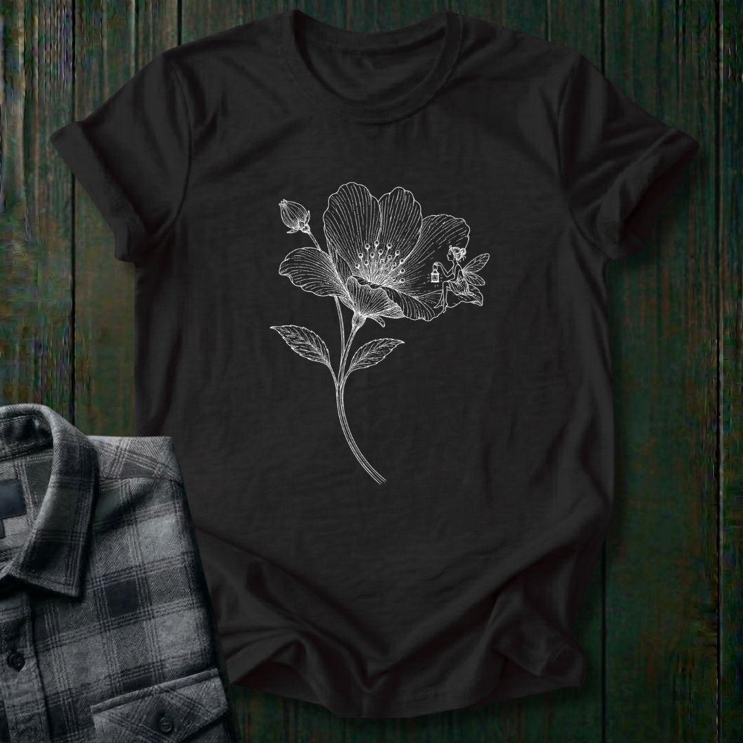 Vintage botanical illustration of a blooming wildflower with a tiny fairy sitting on one petal, surrounded by delicate engraved details and a flower bud on a black tee.