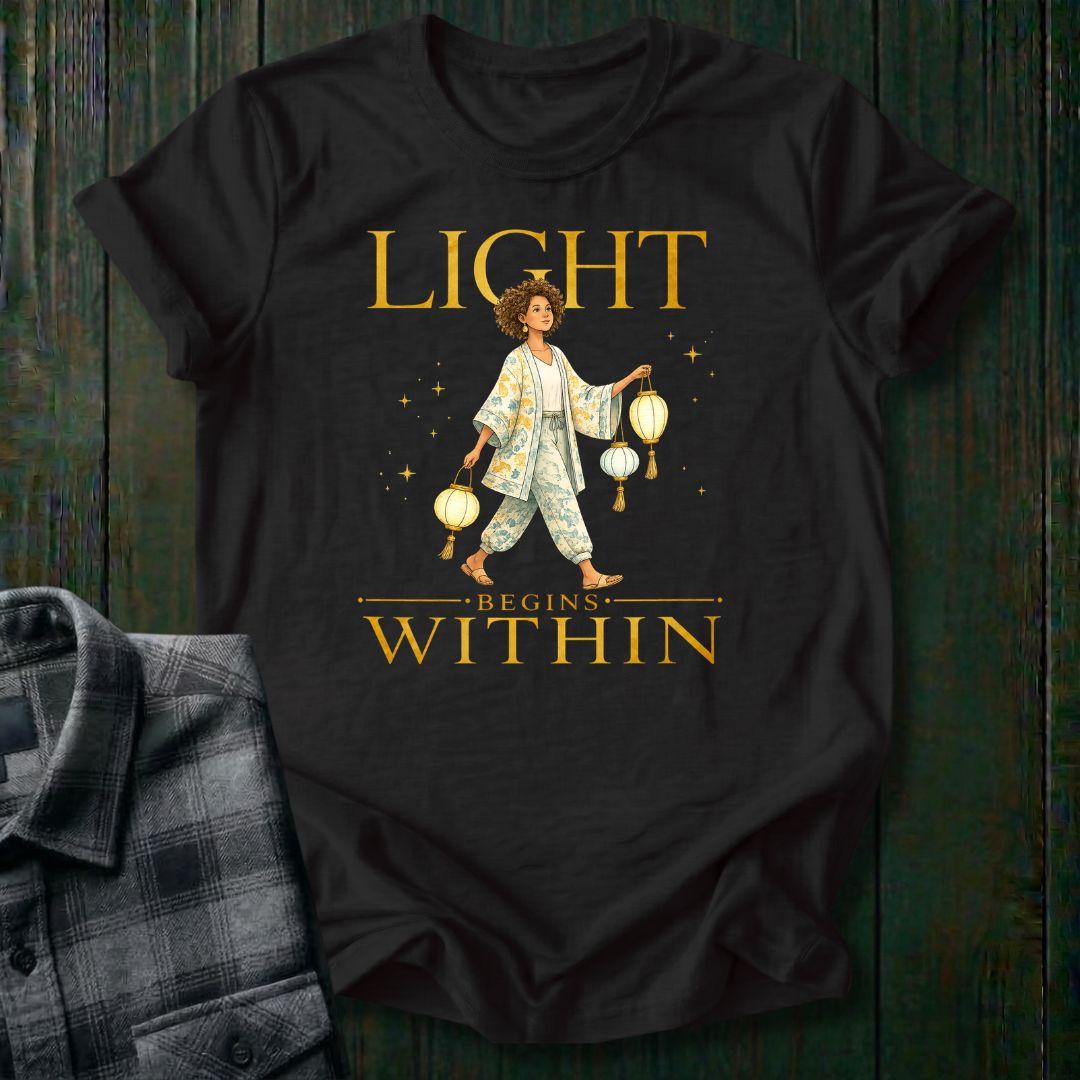Illustrated woman carrying glowing paper lanterns beneath the words "Light Begins Within," symbolizing inner light, hope, mindfulness, and personal growth on a black tee