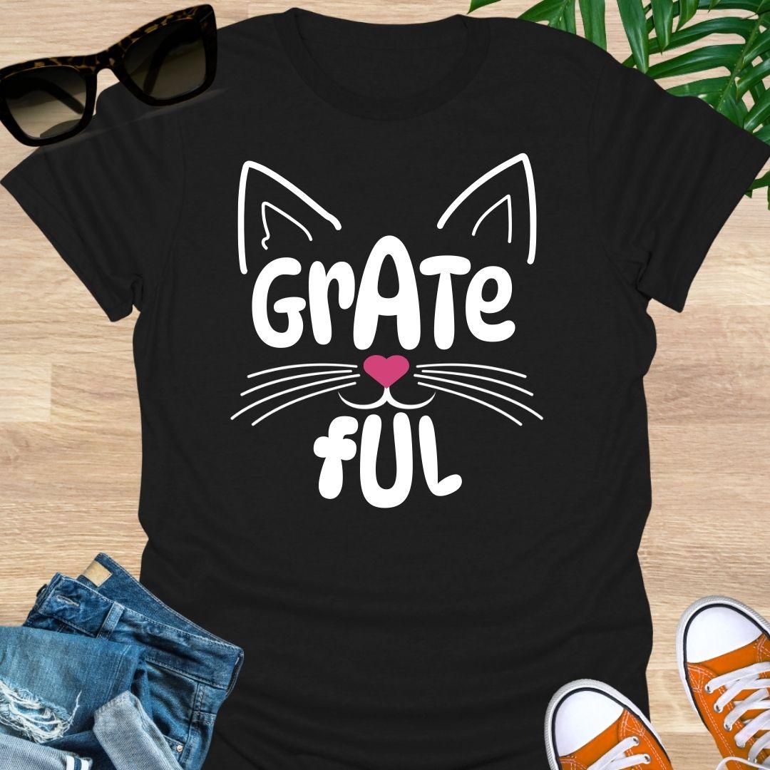 Black unisex graphic t-shirt with cat ears, whiskers, and a pink heart nose forming the word GRATEFUL