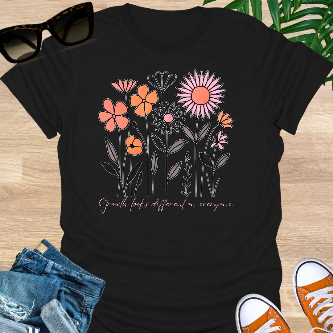 Black unisex t-shirt. Hand-drawn wildflowers with the script “Growth looks different on everyone” 