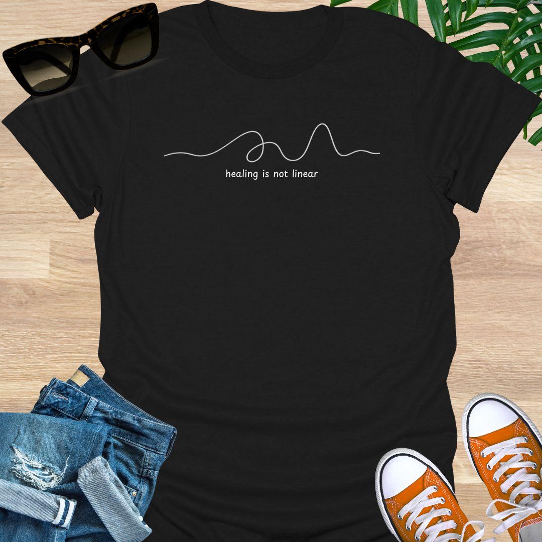 Black unisex t-shirt with minimalist line art and white text reading healing is not linear