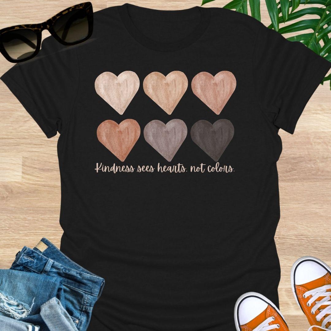 Black t-shirt with six watercolor hearts in diverse skin tones above the script “Kindness sees hearts, not colors” on a unisex tee.