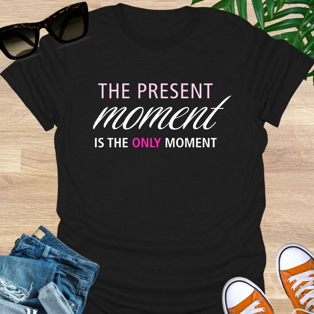 Black tee with pink/white text reading “The Present Moment Is the Only Moment” minimalist mindfulness graphic.