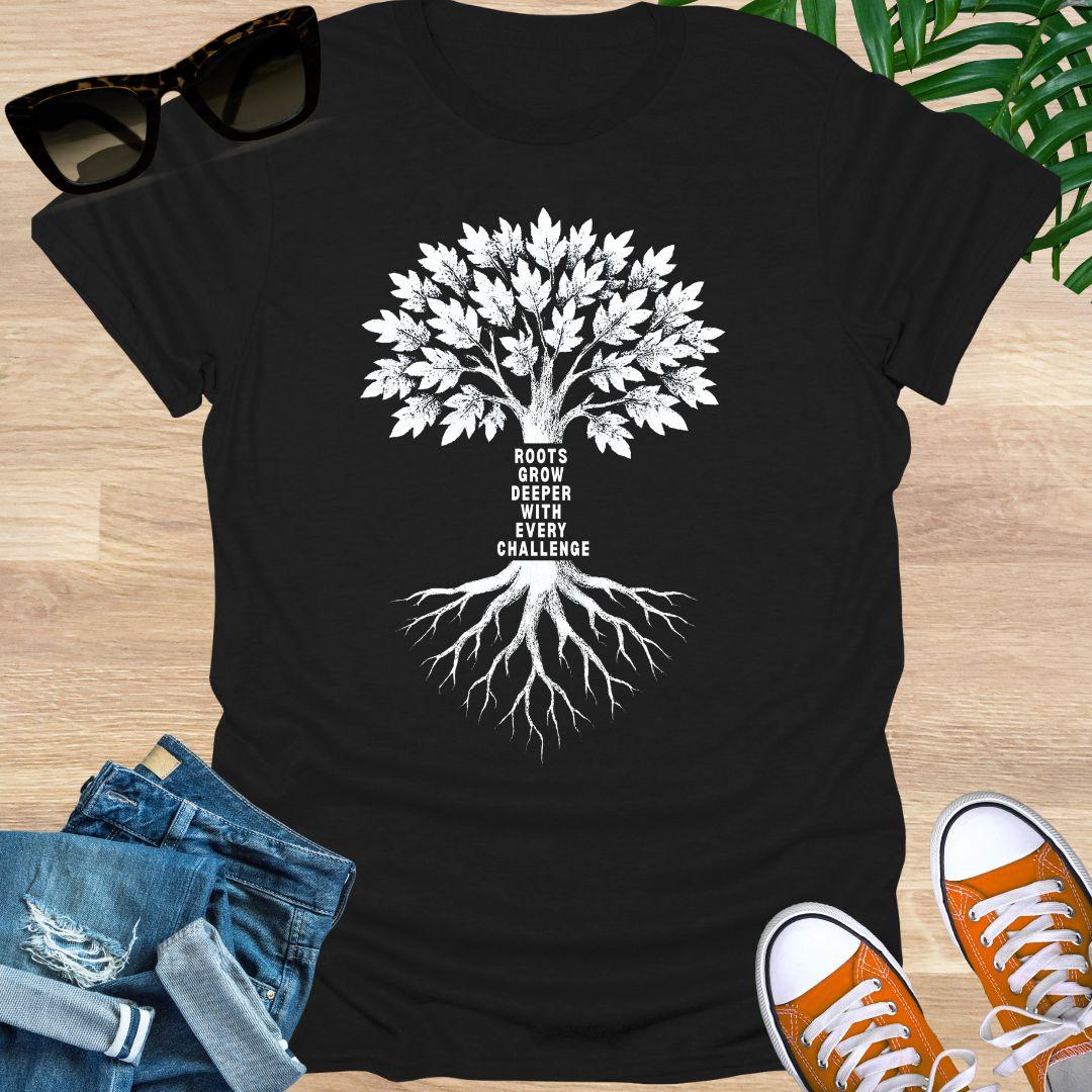White tree with deep roots and the phrase “Roots grow deeper with every challenge” on a black unisex tee.