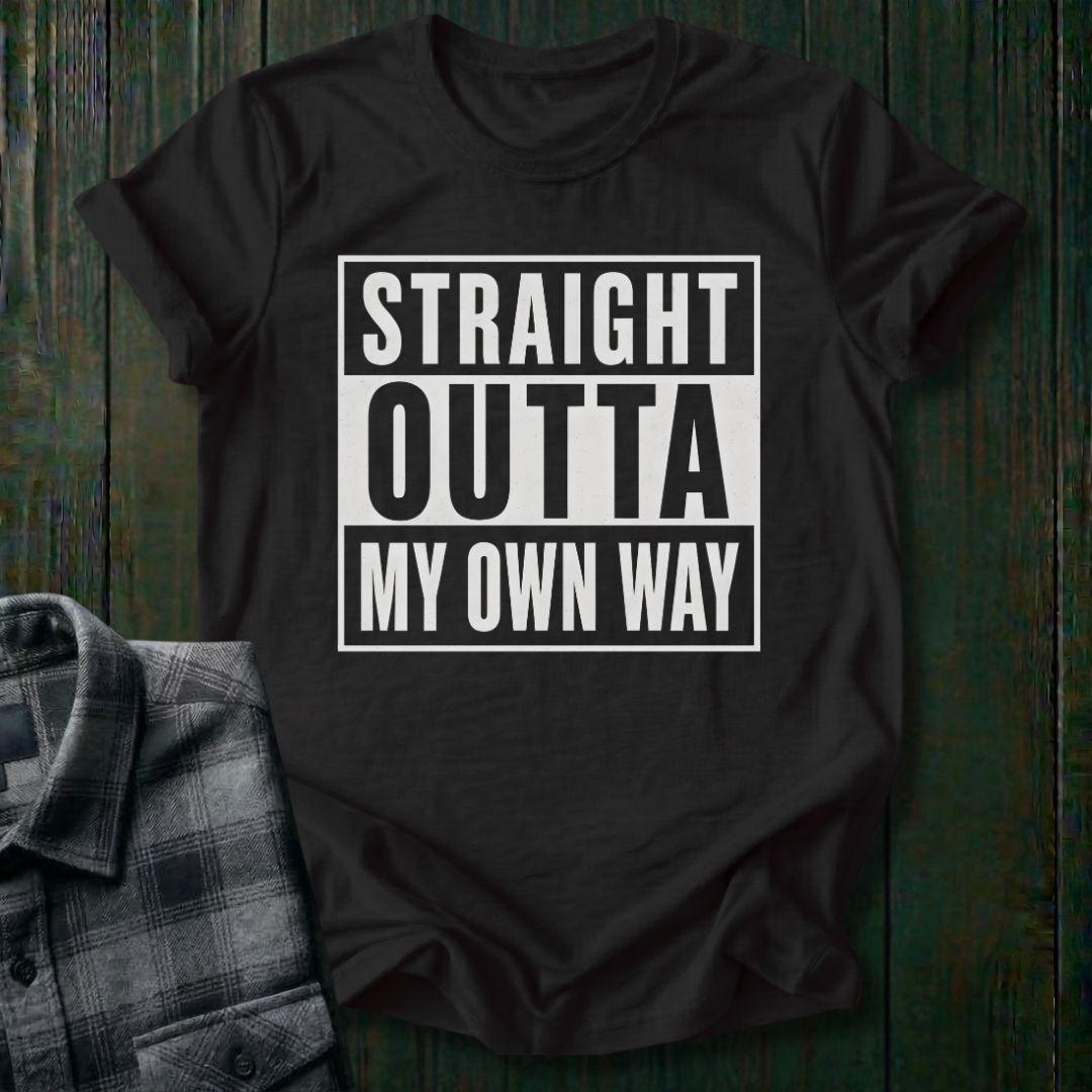Black t-shirt with 'Straight Outta My Own Way' text on a wooden surface with a plaid shirt.