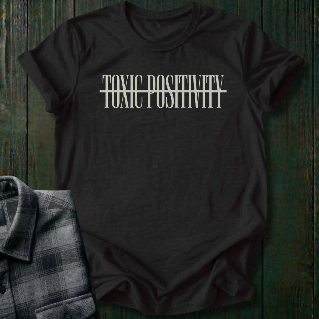 Black tee with minimalist typography design featuring the phrase "No More Toxic Positivity" in bold modern lettering with a horizontal line running through the center of the text.