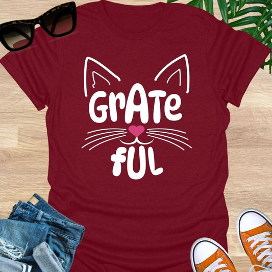 Red unisex graphic t-shirt with cat ears, whiskers, and a pink heart nose forming the word GRATEFUL