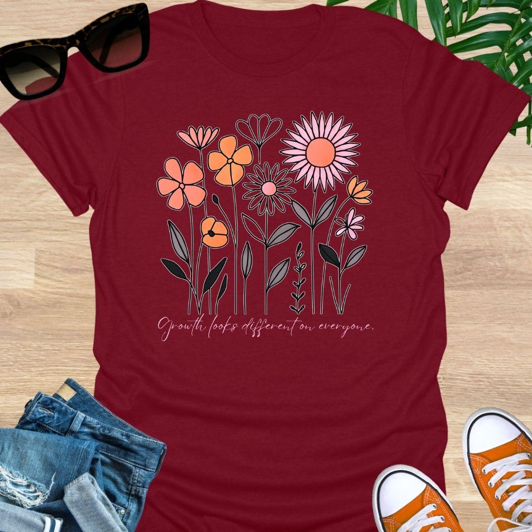 Red unisex t-shirt. Hand-drawn wildflowers with the script “Growth looks different on everyone” 