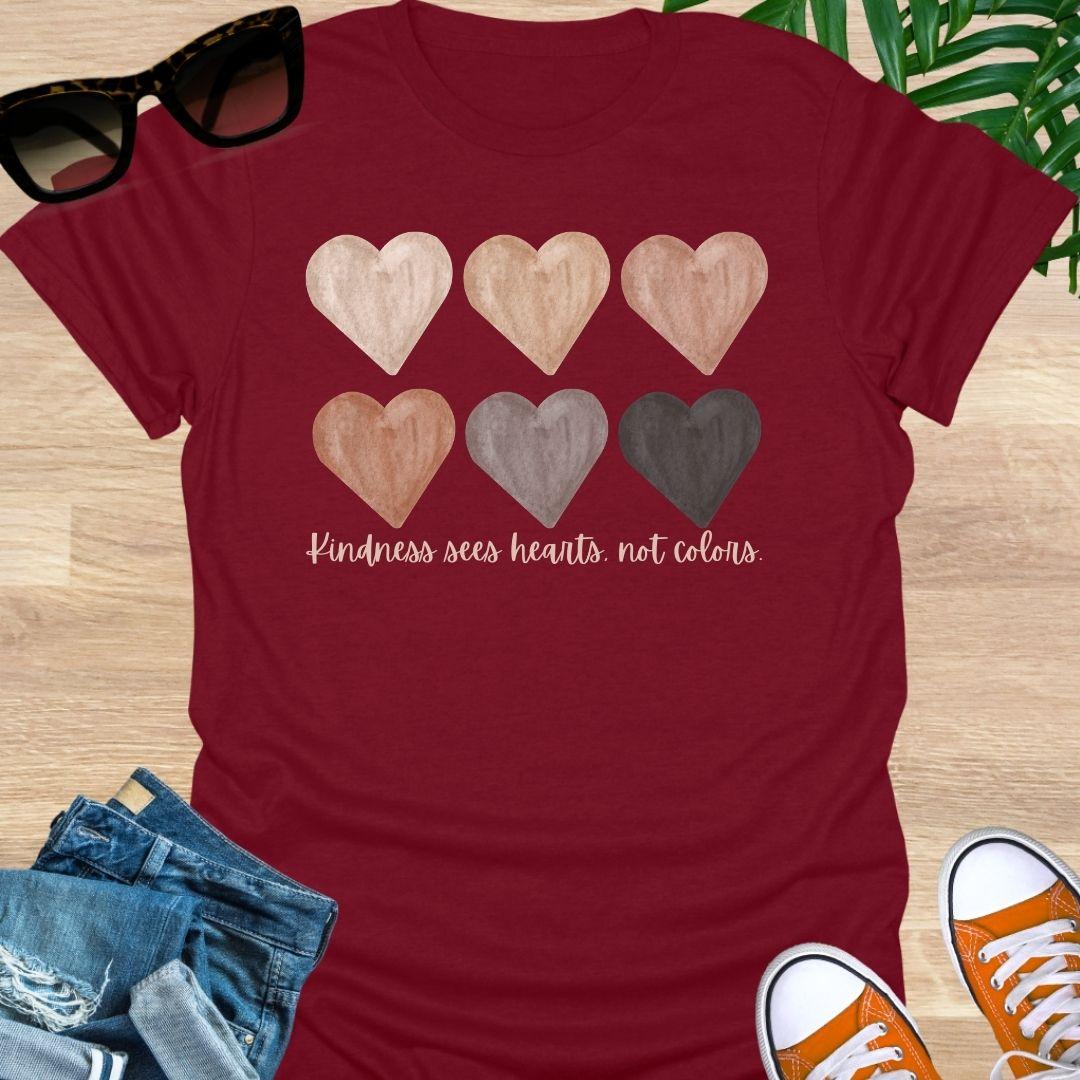 Red t-shirt with six watercolor hearts in diverse skin tones above the script “Kindness sees hearts, not colors” on a unisex tee.