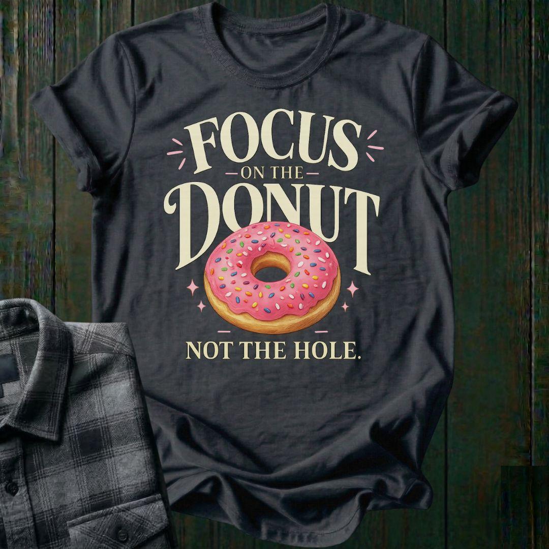 Typography design featuring the phrase "Focus on the Donut, Not the Hole" with a pink sprinkled donut, symbolizing gratitude, perspective, and focusing on life's blessings on a charcoal tee