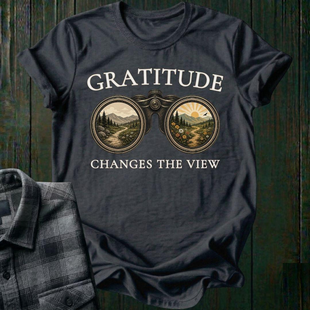 Vintage binoculars graphic showing two landscapes, one ordinary and one bright and colorful, with the phrase "Gratitude Changes the View" on a charcoal tee