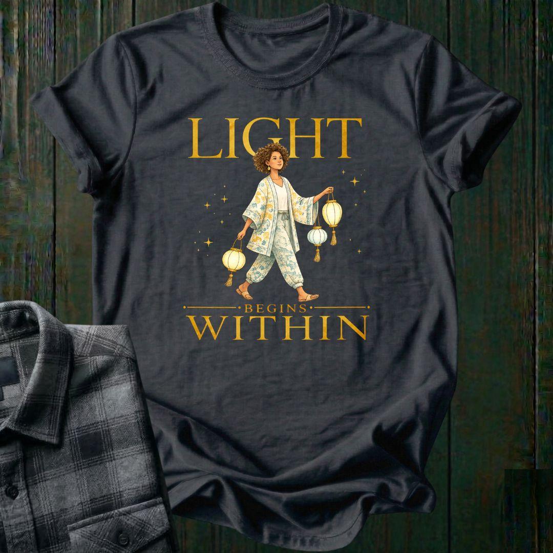 Illustrated woman carrying glowing paper lanterns beneath the words "Light Begins Within," symbolizing inner light, hope, mindfulness, and personal growth on a charcoal tee