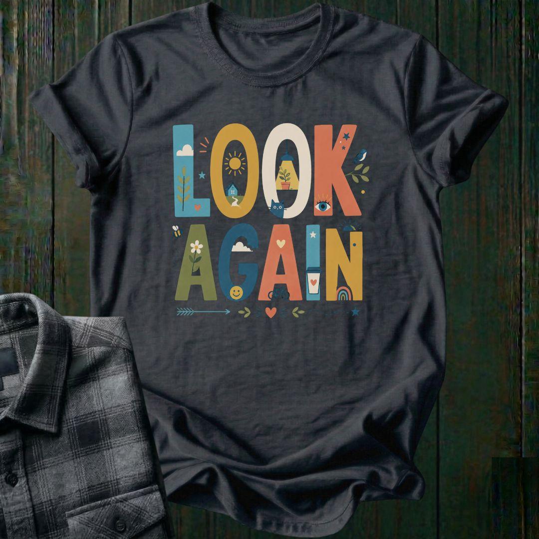 Colorful typography design featuring the phrase "Look Again" filled with cheerful illustrations including a house, sunshine, flowers, coffee cup, bicycle, rainbow, cat, and bird on a charcoal gray tee