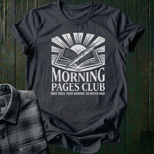 Vintage-style graphic featuring an open journal, pen, and sunrise above the words "Morning Pages Club" with the phrase "Three Pages. Every Morning. No Matter What." on a charcoal tee. 
