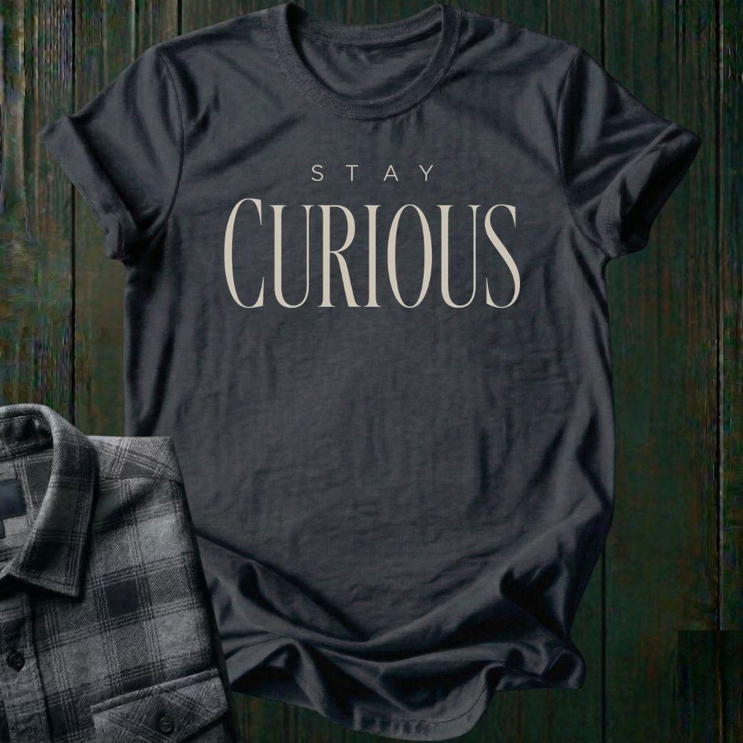 Elegant minimalist typography design featuring the phrase "Stay Curious" in refined serif lettering on a charcoal tee.