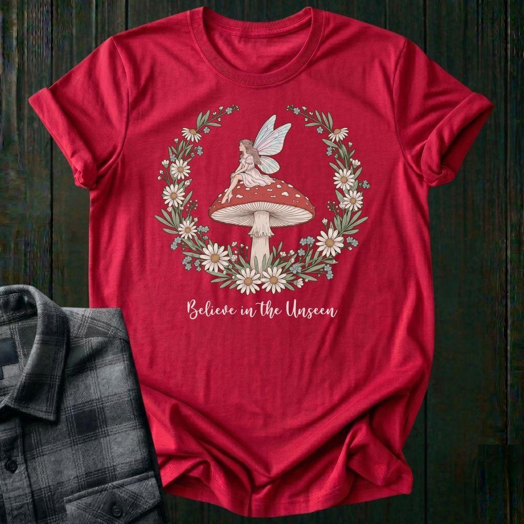 Red t-shirt with fairy and mushroom design on a wooden surface