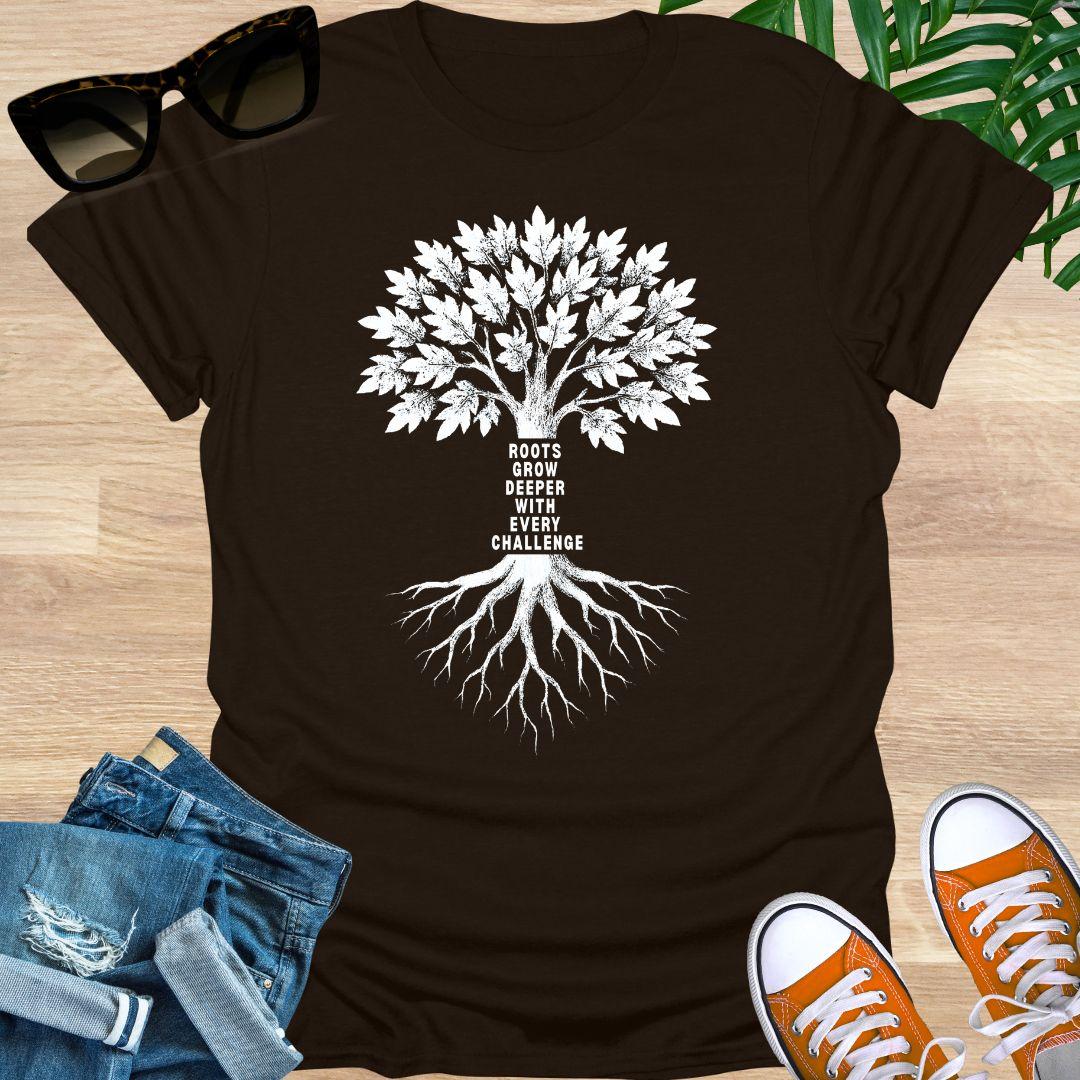 White tree with deep roots and the phrase “Roots grow deeper with every challenge” on a brown unisex tee.