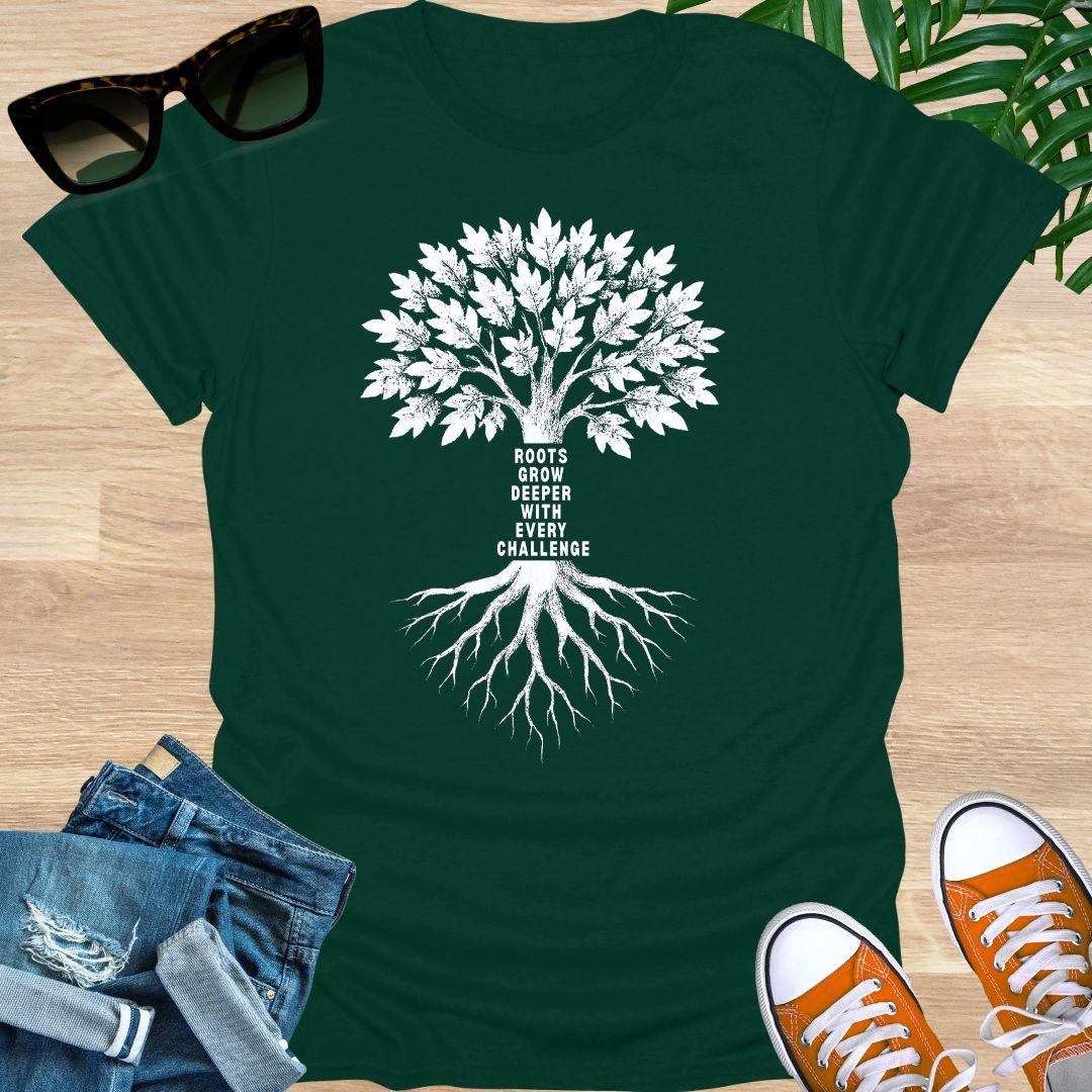 White tree with deep roots and the phrase “Roots grow deeper with every challenge” on a forest green unisex tee.