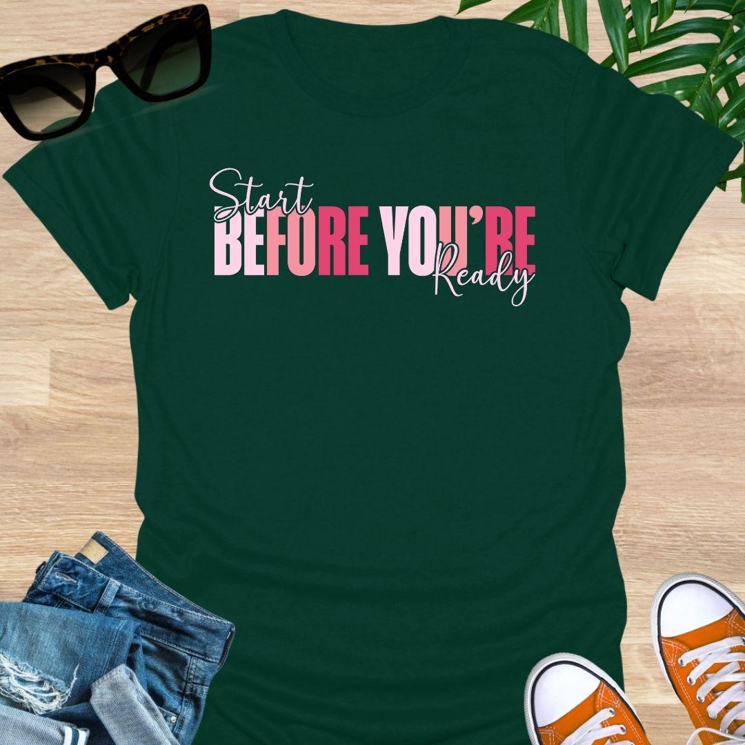 “Start Before You’re Ready” in pink gradient block letters with script overlay on a forest green unisex tee.