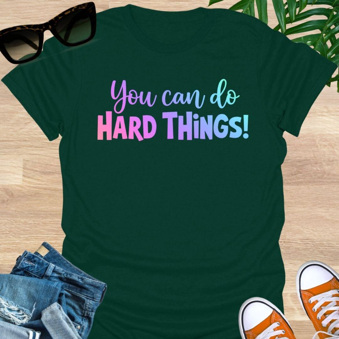 “You Can Do Hard Things” in sunrise gradient lettering on a forest green unisex tee.